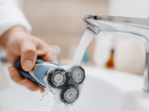 man cleaning electric razor after shaving with water